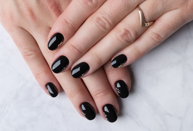 Schöne Frauenhand mit eleganter Maniküre auf Marmorhintergrund. Minimales schwarzes Nageldesign.