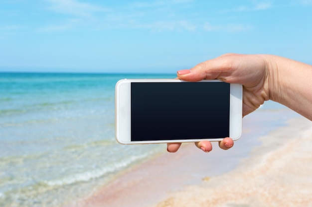 Schöne Frauenhand mit Smartphone am Strand