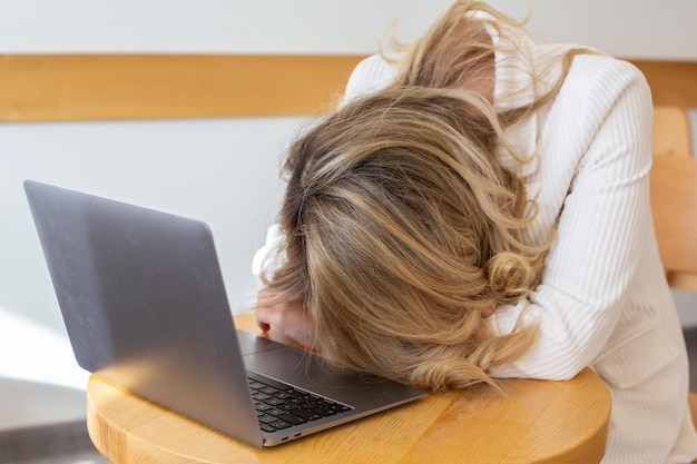 Schöne Freiberuflerin, die sich müde und gestresst fühlt, während sie einen Laptop benutzt und aus der Ferne arbeitet.