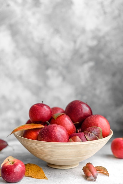 Schöne frische rote Äpfel mit Herbstlaub in einer Holzvase auf einem hellen Betontisch. Erntezeit