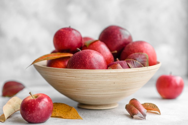 Schöne frische rote Äpfel mit Herbstlaub in einer Holzvase auf einem hellen Betontisch. Erntezeit