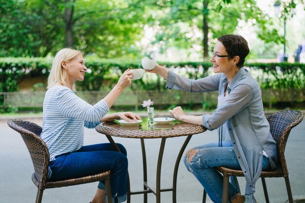 Schöne fröhliche Damen, die Teetassen klirren und im Café im Freien sprechen