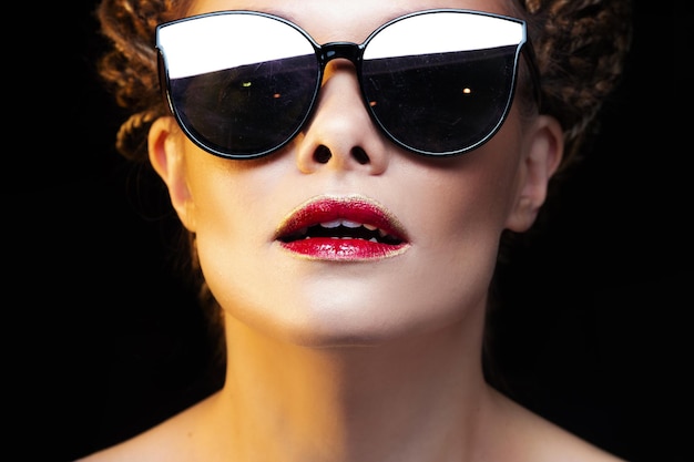 Schöne fröhliche junge Frau mit hellen Lippen der Sonnenbrille mit rotem Lippenstiftporträt auf Schwarzem