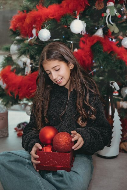 Schöne fröhliche schöne glückliche Brünette Teenager-Mädchen schmückt Weihnachtsbaum rote Weihnachtskugeln.