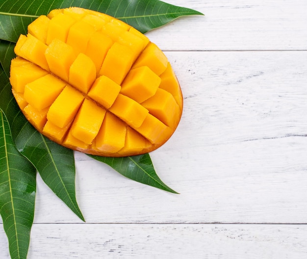 Schöne gehackte Mango mit grünen Blättern auf hellweißem Holzhintergrund Oben Ansicht von oben flach liegender Kopierbereich Nahaufnahme Tropisches Fruchtkonzept