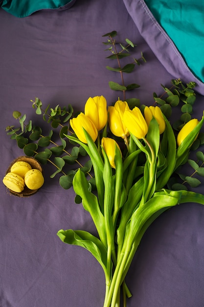 Schöne gelbe Tulpen mit macarons auf Bett