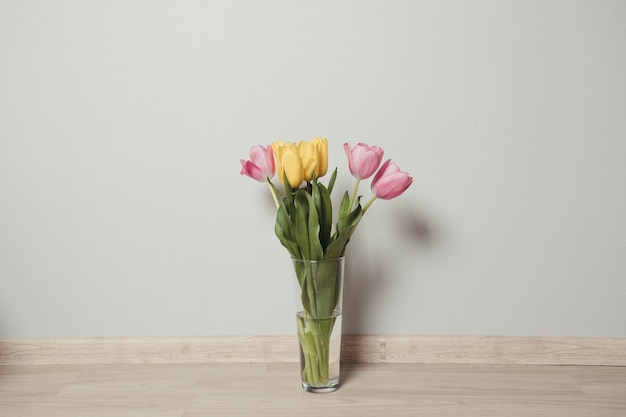 Schöne gelbe und rosa Tulpen in Glasvase auf dem Boden im Raum