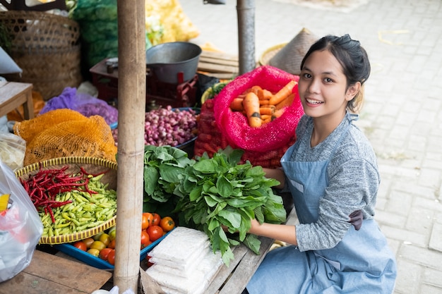 Schöne Gemüsehändlerin arrangiert Spinat für ihre Gemüsestandstandanzeige auf einem traditionellen Markt