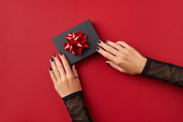 Schöne gepflegte Frauenhände mit Geschenkbox auf rotem Hintergrund Halloween-Shopping-Verkaufskonzept