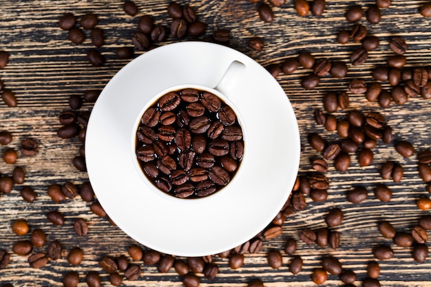 Schöne geröstete Kaffeebohnen mit warmem, frisch zubereitetem Kaffee in einer weißen Tasse, Vollkornprodukte für die Zubereitung von Getränken, enthalten Koffein