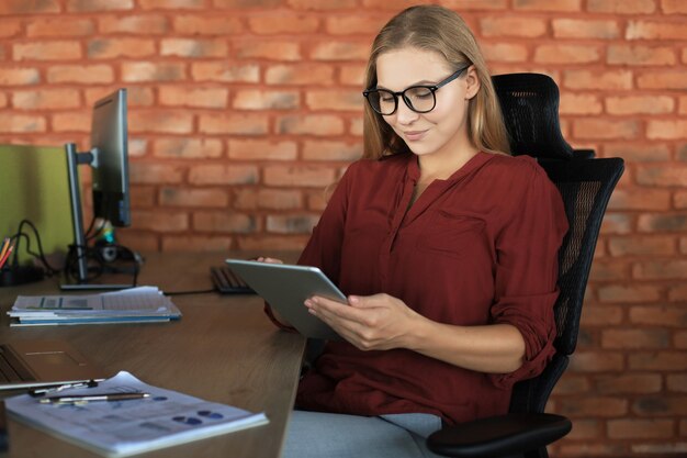 Schöne Geschäftsfrau arbeitet mit digitalem Tablet beim Sitzen im Kreativbüro.