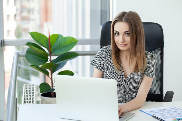 Schöne Geschäftsfrau benutzt einen Laptop und lächelt, während sie im Büro arbeitet