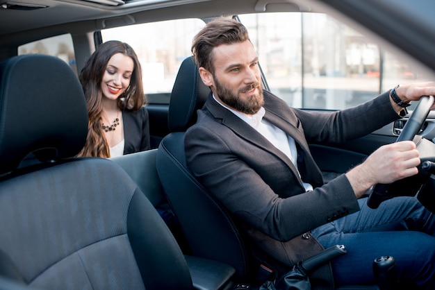 Schöne Geschäftsfrau, die auf dem Rücksitz mit elegantem Mann sitzt, der das Auto in der Stadt fährt