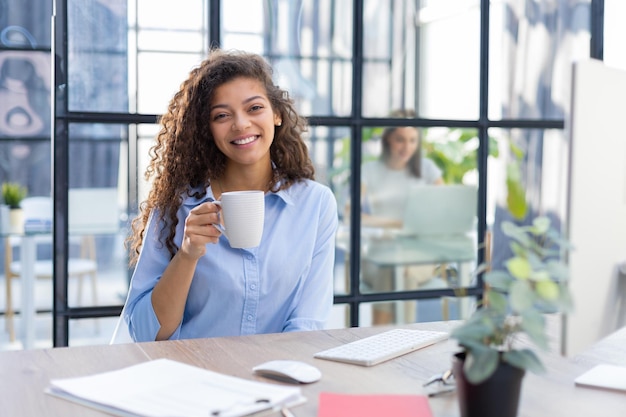 Schöne Geschäftsfrau, die Kaffee trinkt, während sie am Computer arbeitet Kollege ist im Hintergrund