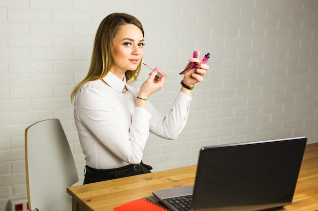 Schöne Geschäftsfrau, die Make-up im Büro anwendet