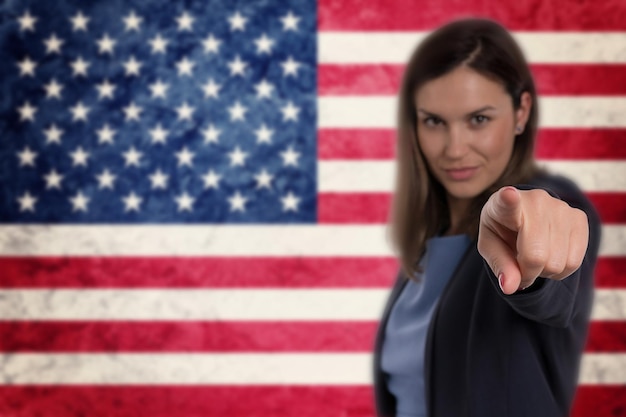 Schöne Geschäftsfrau, die mit dem Finger auf Sie zeigt Hintergrund der USA-Flagge.