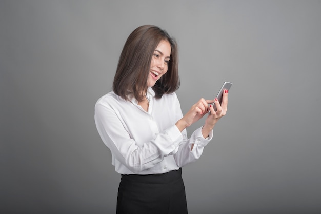Schöne Geschäftsfrau, die Smartphone auf grauem Hintergrund verwendet