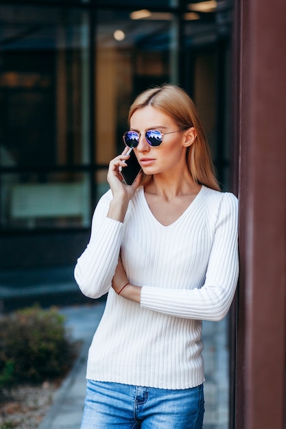 Schöne Geschäftsfrau mit Brille und Telefon auf Straßenhintergrund