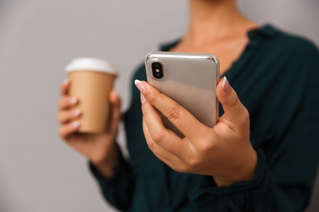 Schöne Geschäftsfrau posiert isoliert über grauem Wandhintergrund Kaffeetrinken per Handy zu sprechen.