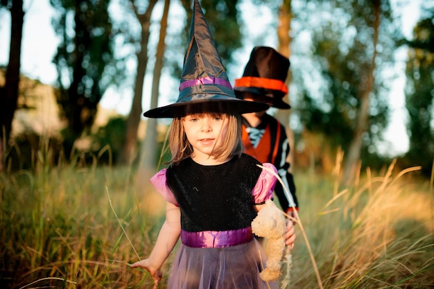 Schöne Geschwister in Kostümen gegen Bäume während Halloween