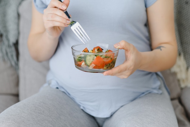 Schöne gesunde schwangere Frau, die Gemüsesalat isst