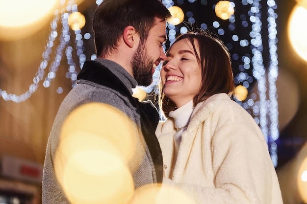 Schöne Girlandenbeleuchtung Glückliches junges Paar feiert Neujahr im Freien auf der Straße