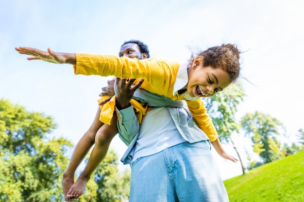 Schöne glückliche afroamerikanische Familie im Park - Schwarze Familie, die Spaß im Freien hat, Vater spielt mit seiner süßen Tochter