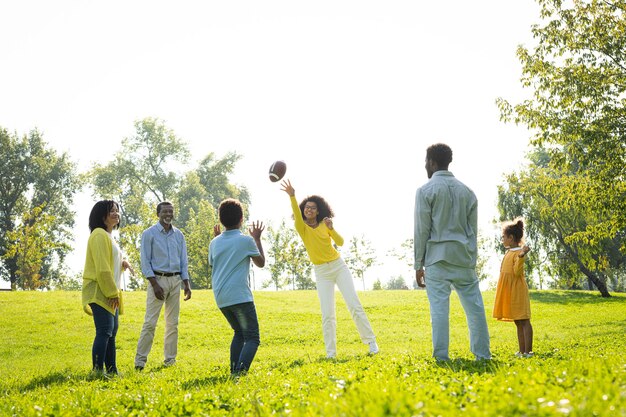 Schöne glückliche afroamerikanische Familienbindung im Park - Schwarze Familie, die Spaß im Freien hat, Eltern und Kinder, die Fußball spielen