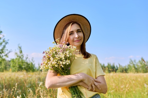 Schöne glückliche erwachsene Frau mit Strauß wilder Blumen auf der Sommerwiese