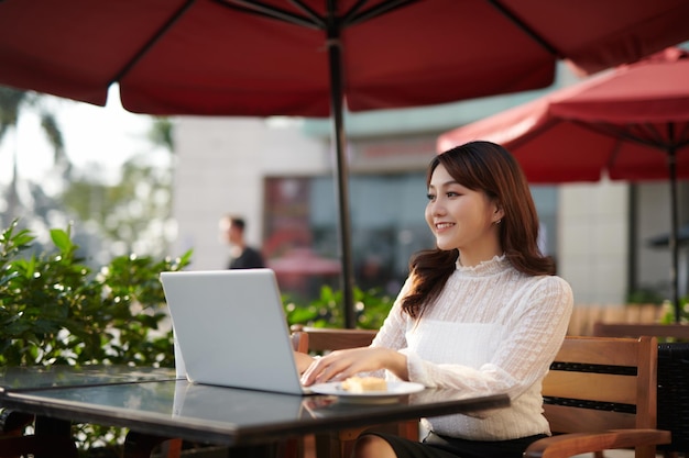 Schöne glückliche Frau, die mit Laptop sitzt