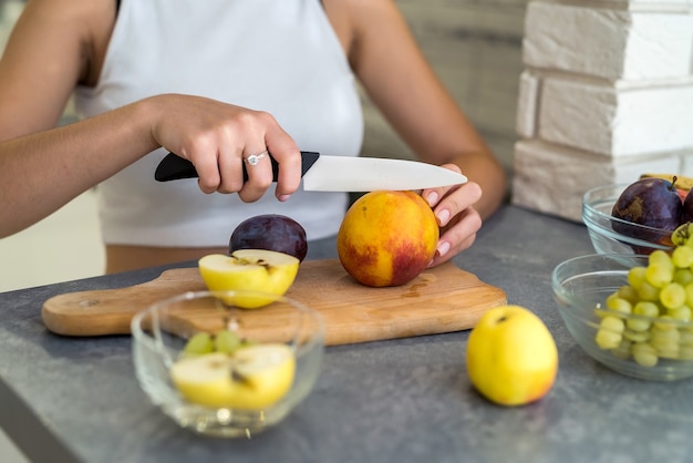 Schöne glückliche Frau in der Küche, die Obstsalat macht. Konzept der gesunden Ernährung