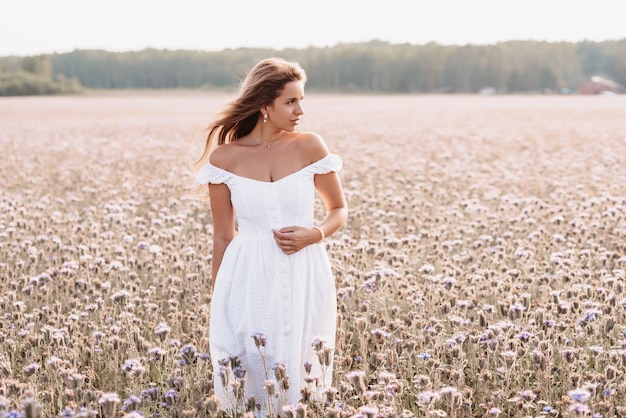 Schöne glückliche Frau in einem weißen Kleid in einem Feld von Blumen im Sommer in der Natur