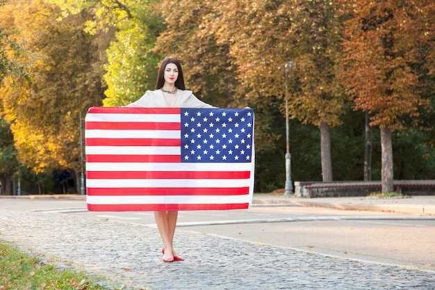 Schöne glückliche Frau mit amerikanischer Flagge, die Unabhängigkeitstag feiert