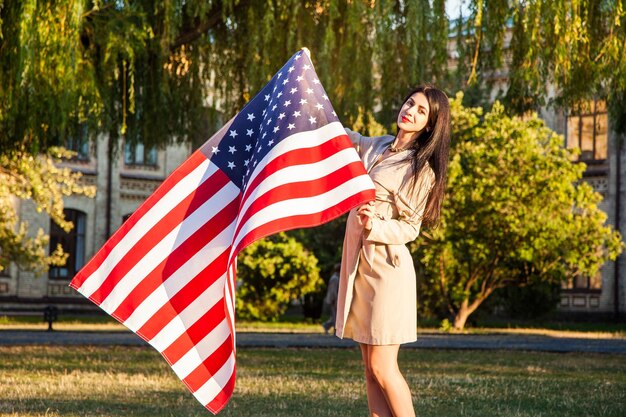 Schöne glückliche Frau mit amerikanischer Flagge, die Unabhängigkeitstag feiert