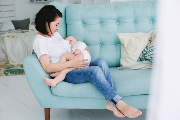 Schöne glückliche junge asiatische Mutter, die ihre Babytochter im Schlafzimmer streichelt