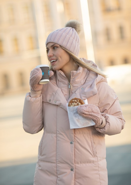 Schöne glückliche junge erwachsene Frau, die Kaffee trägt Winterkleidung trägt und lächelt. Schöne Frau, die Papierkaffeetasse draußen in der Stadt hält.