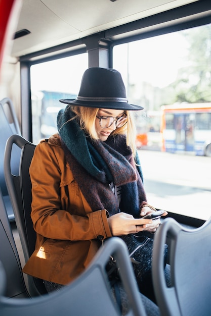 Foto schöne glückliche junge frau, die im stadtbus sitzt und handy betrachtet