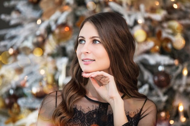 Schöne glückliche junge Frau im schönen Kleid mit Make-up und Frisur in Weihnachtsdekorationen