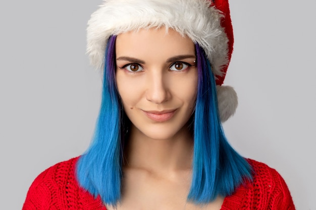 Schöne glückliche junge Frau im Weihnachtsmannhut über grauem Hintergrund. Weihnachtseinkaufsverkaufskonzept