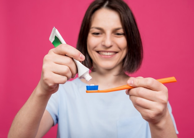 Schöne glückliche junge Frau mit Zahnbürste auf leerem rosa Hintergrund