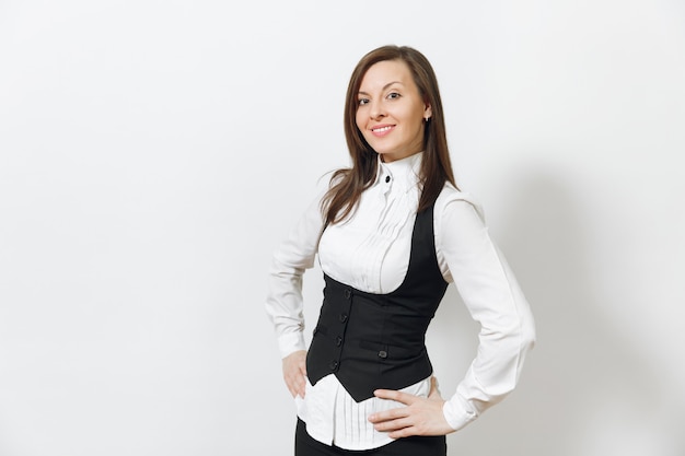 Schöne glückliche kaukasische junge lächelnde braunhaarige Geschäftsfrau im schwarzen Anzug, weißes Hemd, das Kamera lokalisiert auf weißer Wand schaut