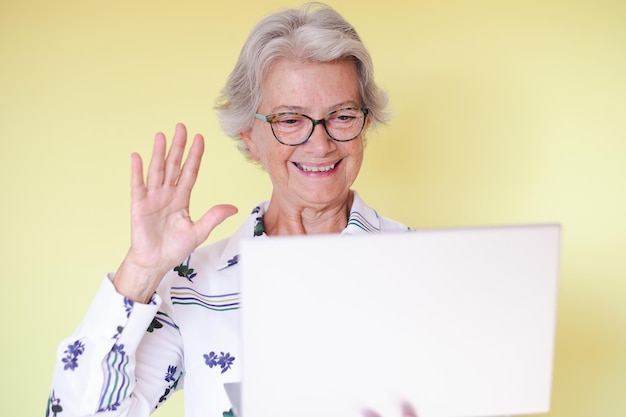 Schöne glückliche Seniorin im Video-Chat mit Laptop auf gelbem Hintergrund