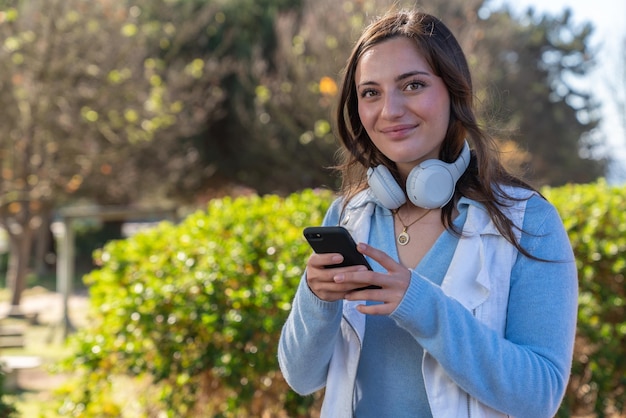 Schöne glückliche Teenagerin, die nachmittags ihr Handy in einem Park benutzt