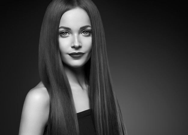 Schöne Haarfrau lange glatte Brunettefrisurschönheit gesundes Haar weibliches vorbildliches Porträt. Studioaufnahme. Einfarbig. Grau. Schwarz und weiß.