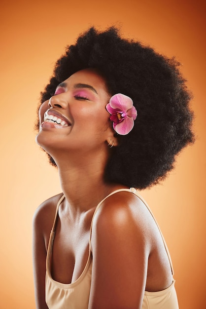 Schöne Hautpflege und schwarze Frau mit Blume im Afro-Haar, die Make-up-Kosmetik trägt und glücklich ist, während sie lacht und mit der Kosmetikbehandlung zufrieden ist Afrikanisches weibliches Modell vor braunem Hintergrund