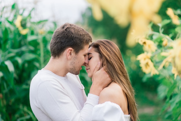 Schöne herrliche Frau und stilvolles hübsches männliches, rustikales Paar in einem Sonnenblumenfeld, das zärtlich küsst
