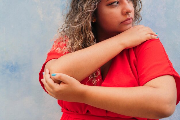 Schöne hispanische Frau im Kleid, das gegen blaue Wand steht