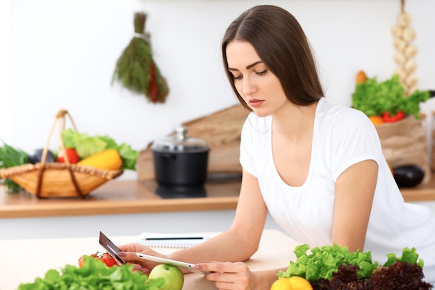 Schöne hispanische Frau macht Online-Shopping per Tablet-Computer und Kreditkarte. Hausfrau fand neues Rezept zum Kochen in einer Küche