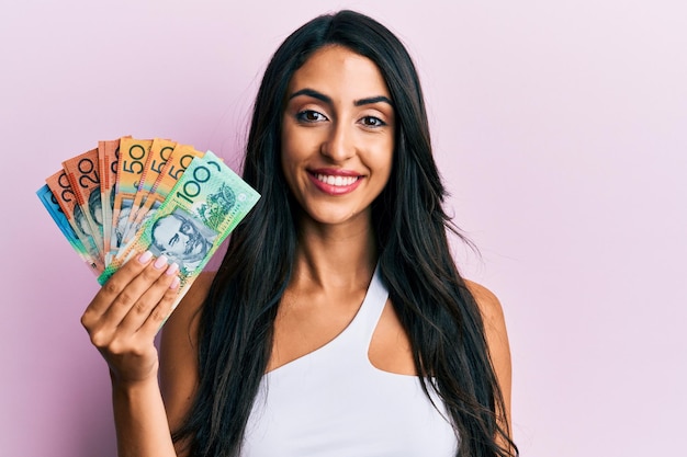 Schöne hispanische Frau mit australischen Dollar, die positiv und glücklich aussieht und mit einem selbstbewussten Lächeln lächelt, das Zähne zeigt