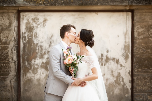 Schöne Hochzeitspaare, die nahe der alten Wand küssen